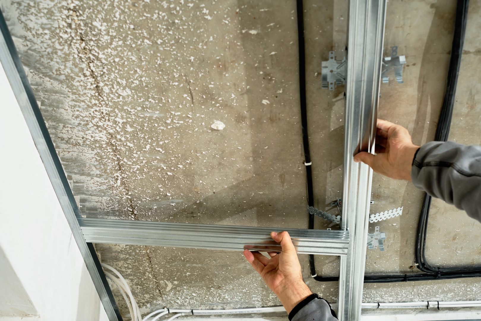 Worker adjusts a metal profile for mounting a plasterboard ceiling frame, close-up, selective focus on the hands of a specialist. Industrial renovation and renovation